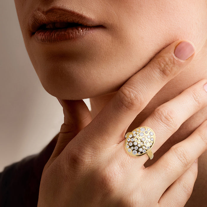 Gold oval diamond ring worn on finger, scattered round stones in circular face