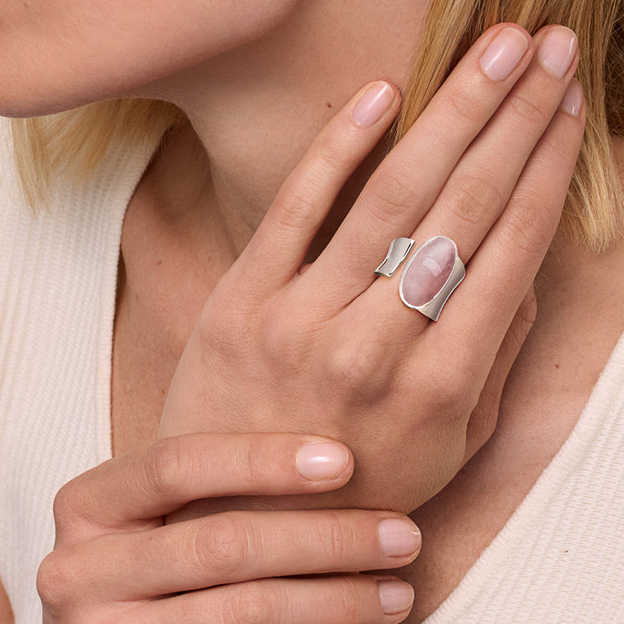 Rose quartz oval wrap ring on finger in sterling silver; pale pink gemstone bezel.