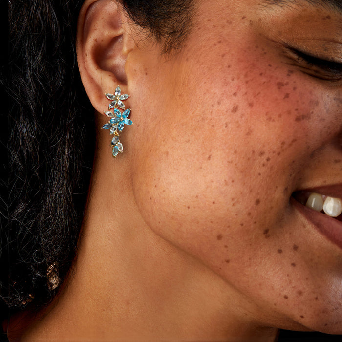 Gold-tone blue gemstone floral drop earrings worn on ear