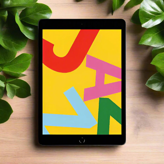 An Apple iPad 7th Gen A2197 10.2" 32GB WiFi Black rests on a wooden surface amid green leaves, its vivid abstract display featuring bold red, pink, blue, and green letters over a yellow background. AU stock, Apple tablet with warranty.