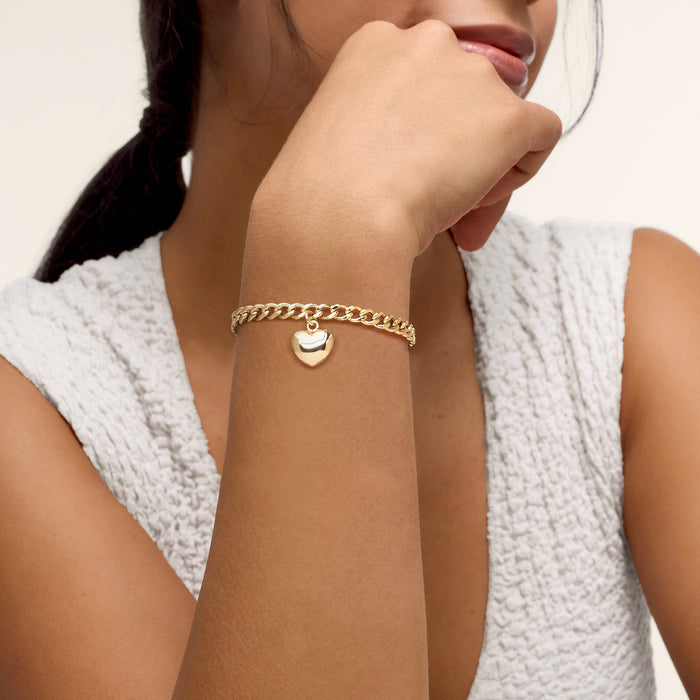 Gold curb-link bracelet on wrist with small puffy heart charm at center