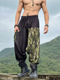A man standing on a elevated road wearing camouflage military camo harem print harem pants with an elastic waistband and drawstrings.