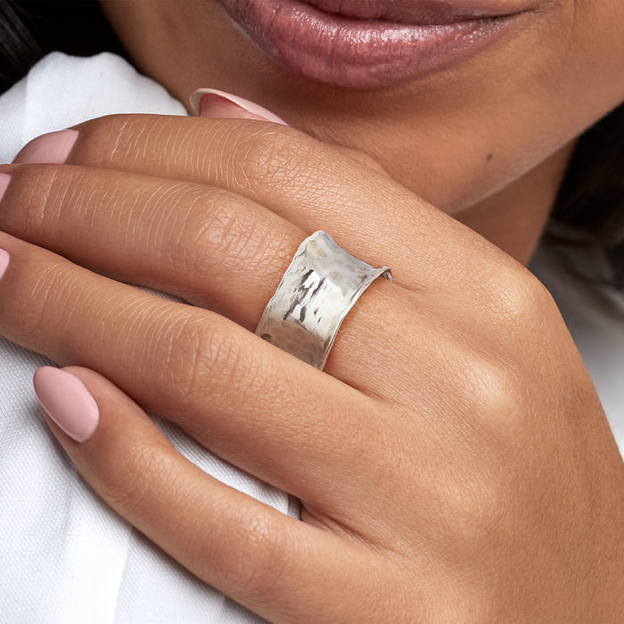 Hammered sterling silver ring on finger, wide textured band with reflective facets.